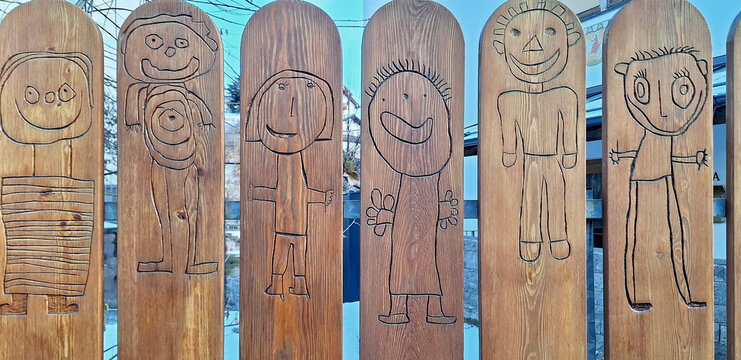 Children's drawings in the form of figures are burned into the fence in the kindergarten. Panorama.