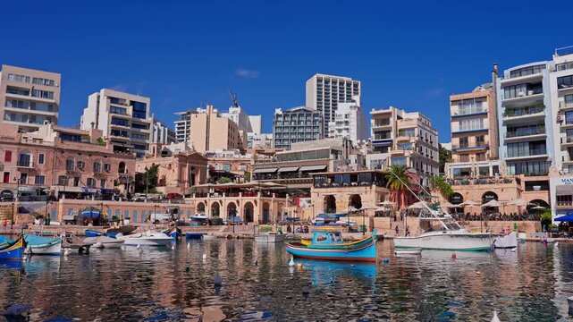 Panoramic midday view in Malta, Sliema town, shows luzzu boats and yachts, limestone colonnades, cafes, and modern blocks. Boats bob, water ripples, people move along the quay.
