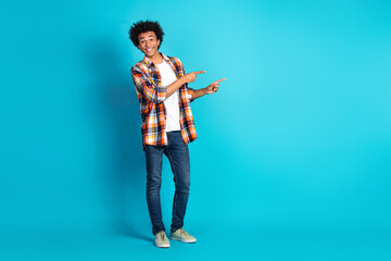 Young man in casual plaid shirt points and smiles against blue studio backdrop for lifestyle...