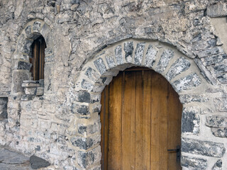 Fototapeta premium Rustic stone entrance with wooden door and arched window in vintage architecture