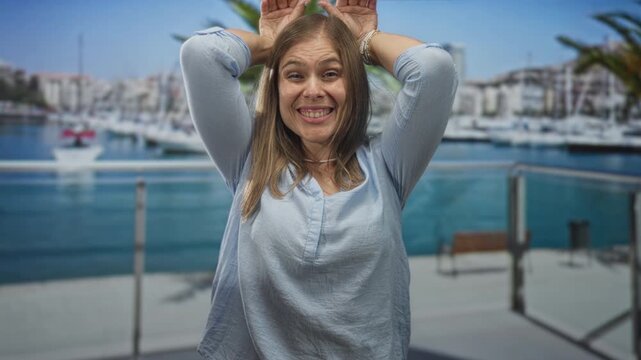 Woman raises her hands above her head and smiles on a boat deck at a port; spontaneity joy freedom energy.