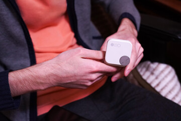 Person holding a compact electronic device with a round button, examining its features. The focus is on the hands and device, highlighting interaction and technology engagement.