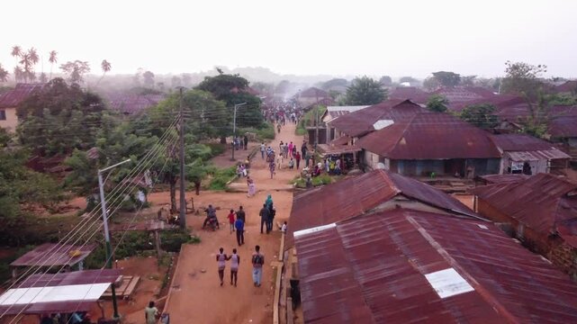 Akure, Nigeria - 27 August 2025: Aerial view of a dusty street bisecting buildings with rusty roofs, and a large crowd gathering in the heart of the town.