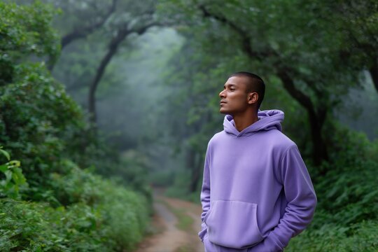 Young hispanic male enjoying peaceful forest walk in purple hoodie