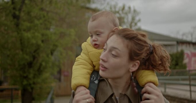A mother gives her toddler a piggyback ride at the zoo as they look at a map and point to animals. This is a heartwarming scene of family bonding.
