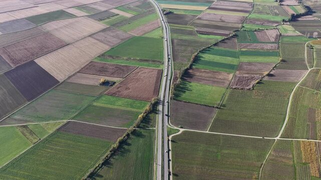 Aerial view of patchwork agricultural fields with diverse colors and textures, bisected by a grey road, Rouffach, Grand Est, France.