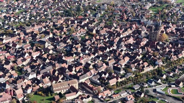 Aerial view of the historic Saint Arbogast Church and tightly packed buildings with contrasting red and brown roofs, Rouffach, Grand Est, France.