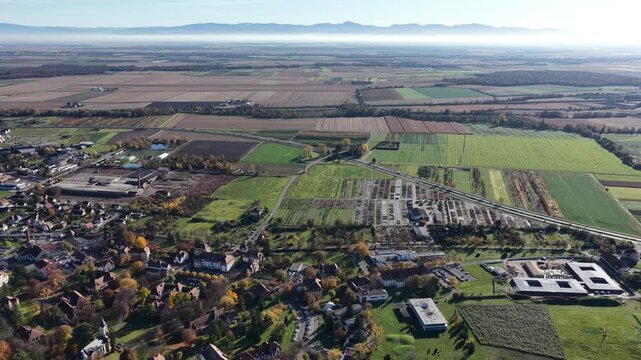 Aerial view of the picturesque landscape with colorful agricultural fields, roads, and scattered buildings under a clear sky, Rouffach, Grand Est, France.