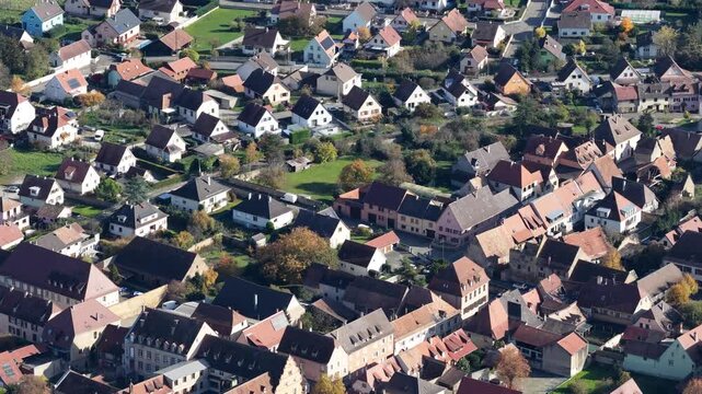 Aerial view of closely packed buildings with red and grey roofs contrasting with green trees and grass, creating a dense urban landscape, Rouffach, Grand Est, France.