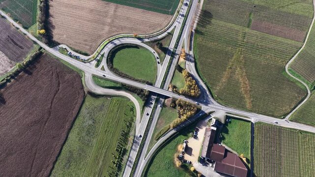 Aerial view of a highway interchange amidst a landscape of fields with varied textures and colors, creating a captivating contrast, Rouffach, Grand Est, France.