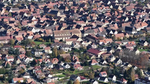 Aerial view of a densely packed town featuring a prominent church amidst the red-roofed buildings under the daylight, Rouffach, Grand Est, France.