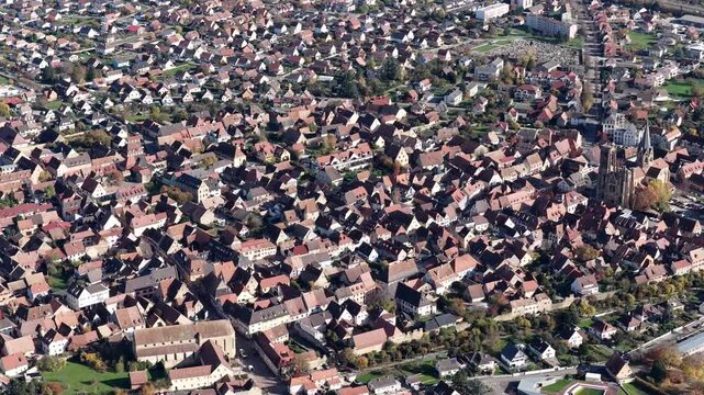 Aerial view of tightly packed buildings with red roofs contrasting with the tall church in the town center, Rouffach, Grand Est, France.