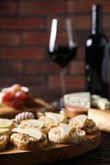 Different tasty bruschettas and red wine on wooden table against brick wall, closeup