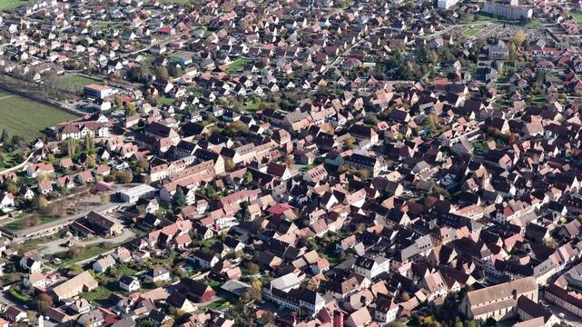 Aerial view of a densely packed town, showcasing red-tiled roofs contrasting with the green trees and fields, creating a textured landscape, Rouffach, Grand Est, France.