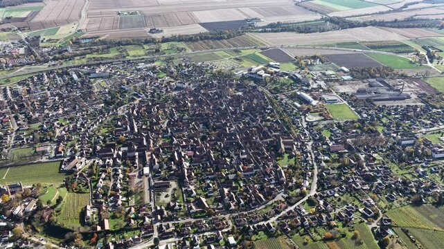 Aerial view of the town with tightly packed buildings contrasting with the surrounding fields in autumn colors, Rouffach, Grand Est, France.