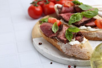 Delicious bruschettas with roast beef served on white tiled table, closeup. Space for text
