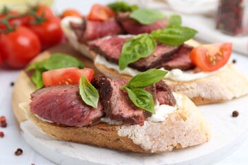 Delicious bruschettas with roast beef served on white table, closeup
