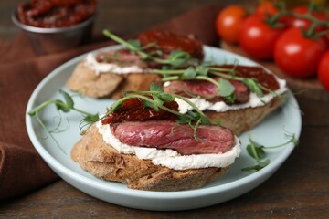 Delicious bruschettas with roast beef served on wooden table, closeup