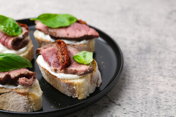 Bruschettas with roast beef, cream cheese, basil and sun-dried tomato on grey table, closeup. Space for text