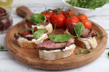 Bruschettas with roast beef served on white wooden table, closeup