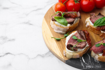 Bruschettas with roast beef, cream cheese, basil, sun-dried tomatoes and fresh vegetables on white marble table, closeup. Space for text