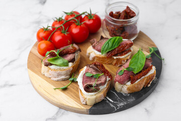 Bruschettas with roast beef, cream cheese, basil, sun-dried tomatoes and fresh vegetables on white marble table, closeup
