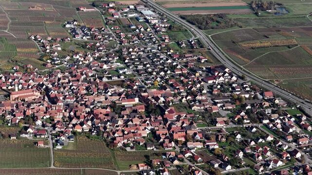 Aerial view of the town of Rouffach, with its red-roofed buildings nestled amidst vineyards and a highway cutting through the landscape, Rouffach, Grand Est, France.