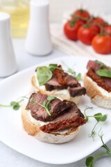 Bruschettas with roast beef, cream cheese, basil, sun-dried tomatoes and fresh vegetables on light grey table, closeup