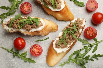 Delicious bruschettas with tuna, tomatoes and arugula on grey table, flat lay