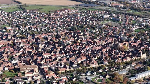 Aerial view of a European town featuring a prominent church with red-tiled roofs contrasting with green spaces, Rouffach, Grand Est, France.