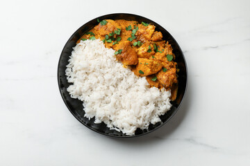 Chicken tikka masala with rice and parsley in bowl on white marble table, top view