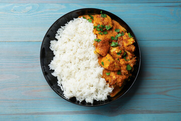 Chicken tikka masala with rice and parsley in bowl on light blue wooden table, top view