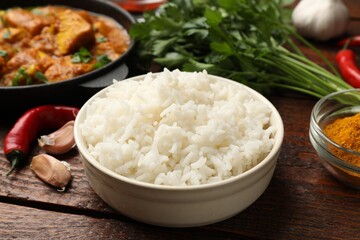 Cooked rice, chicken tikka masala and spices on wooden table, closeup