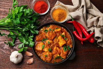 Chicken tikka masala with spices on wooden table, flat lay