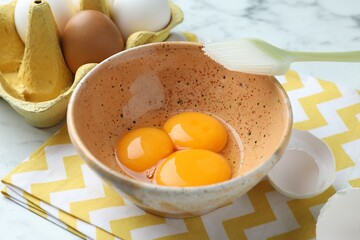 Raw eggs, yolks and brush on white marble table, closeup