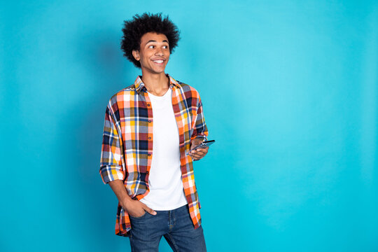 Young man in colorful plaid shirt smiles while holding smartphone against blue background