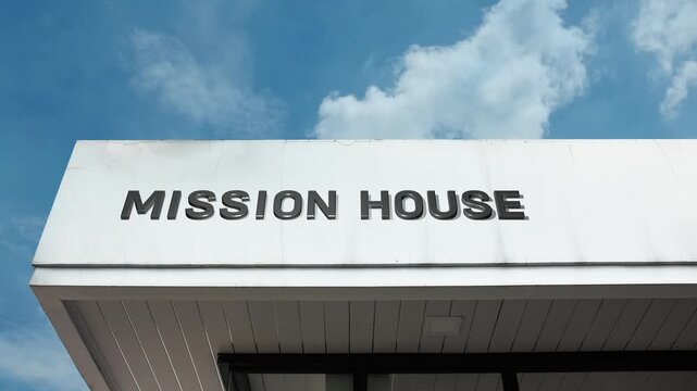 A mission house word sign displayed on a religious or charity building under a clear blue sky, symbolizing outreach, community aid, spiritual work, and support