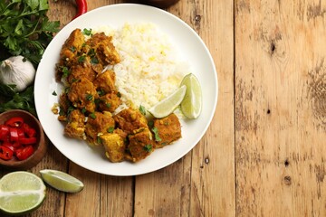Delicious chicken tikka masala with rice, parsley, lime and spices on wooden table, flat lay. Space for text