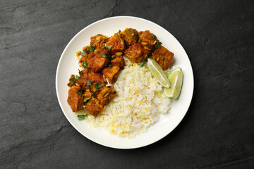 Delicious chicken tikka masala with rice, parsley and lime on dark textured table, top view
