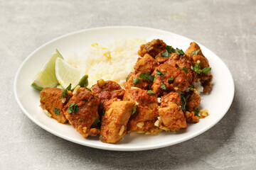 Delicious chicken tikka masala with rice, parsley and lime on grey textured table, closeup