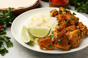 Delicious chicken tikka masala with rice, parsley and lime on grey textured table, closeup
