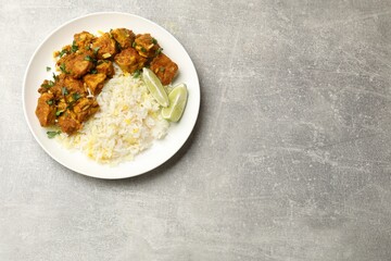 Delicious chicken tikka masala with rice, parsley and lime on grey textured table, top view. Space for text