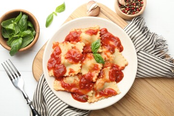 Delicious ravioli with tomato sauce and basil served on white wooden table, flat lay