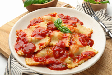 Delicious ravioli with tomato sauce and basil served on white wooden table, closeup