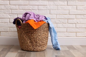 Laundry basket full of clothes on floor near white brick wall indoors. Space for text