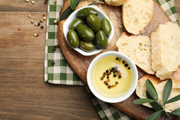 Ciabatta slices, oil with peppercorns and olives on wooden table, flat lay