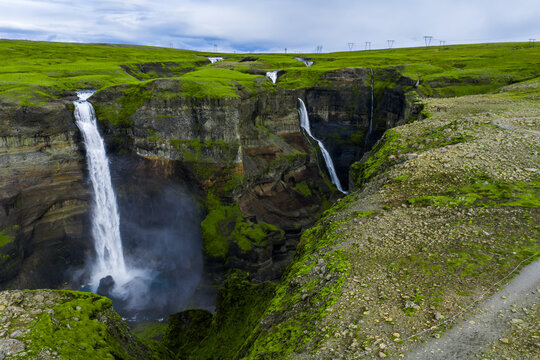 Haifoss and Granni Falls pour into a misty gorge in Thjorsardalur, Iceland. Mossy lava cliffs, layered rock, and a rim track lead the eye under soft overcast light. Stranger Things waterfall.