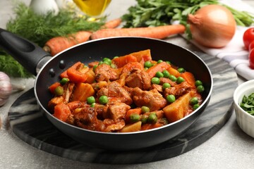 Delicious cooked stew in frying pan and ingredients on grey table, closeup
