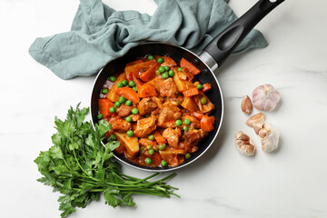 Delicious cooked stew in frying pan, parsley and garlic on white marble table, flat lay