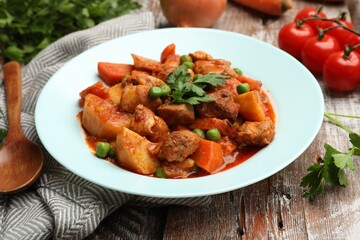 Delicious cooked stew and ingredients on wooden table, closeup
